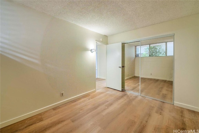 unfurnished bedroom featuring a closet, a textured ceiling, baseboards, and wood finished floors