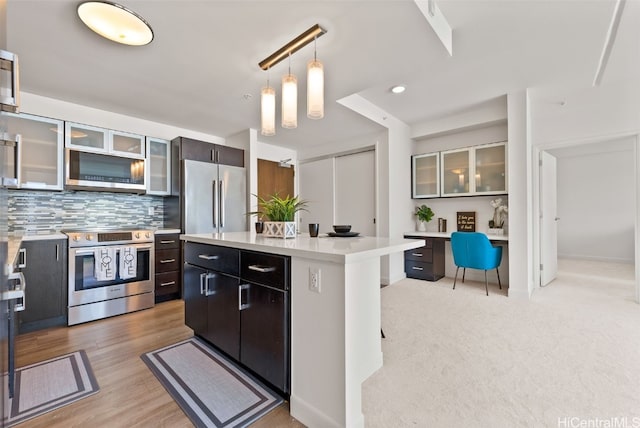 kitchen with appliances with stainless steel finishes, decorative light fixtures, light countertops, built in desk, and backsplash