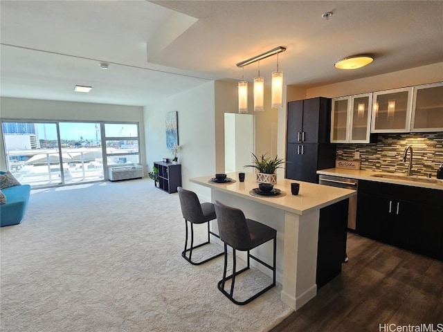 kitchen featuring a sink, a kitchen breakfast bar, light countertops, stainless steel dishwasher, and decorative backsplash