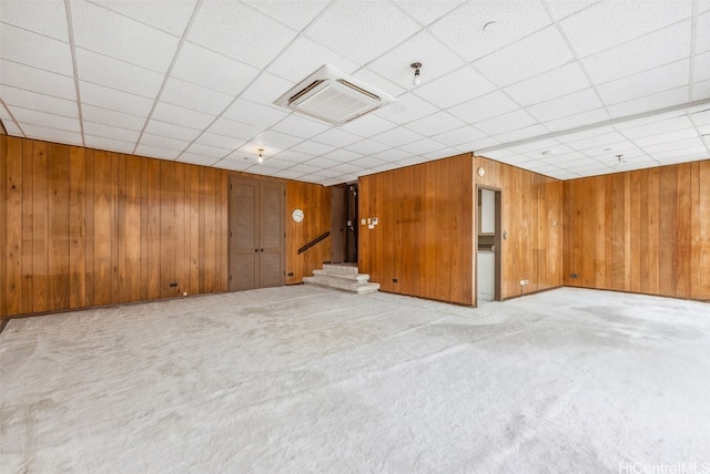 carpeted spare room featuring a drop ceiling, wooden walls, and stairs