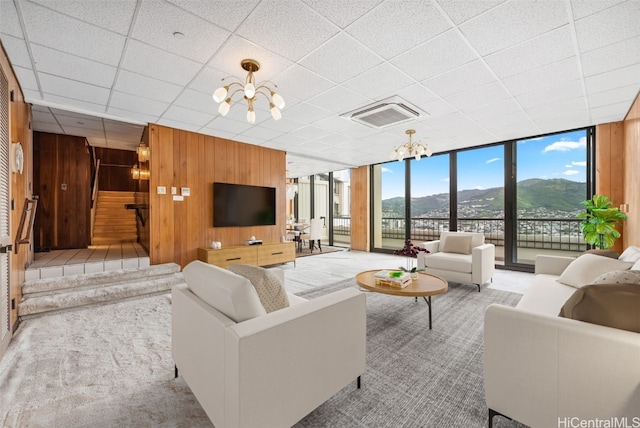 carpeted living room featuring expansive windows, wooden walls, visible vents, and an inviting chandelier