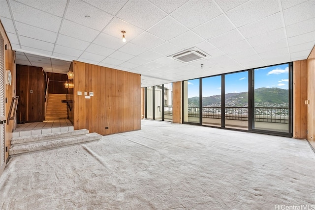 empty room with carpet floors, wood walls, visible vents, and a wall of windows