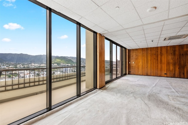 unfurnished room featuring visible vents, a drop ceiling, a wall of windows, wood walls, and a mountain view