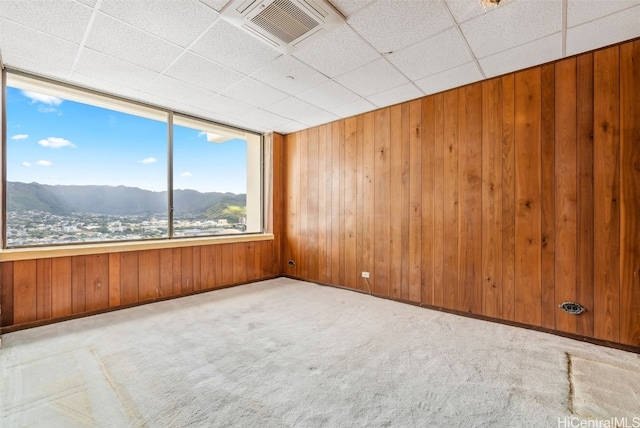 carpeted spare room featuring a mountain view, a paneled ceiling, wood walls, visible vents, and baseboards