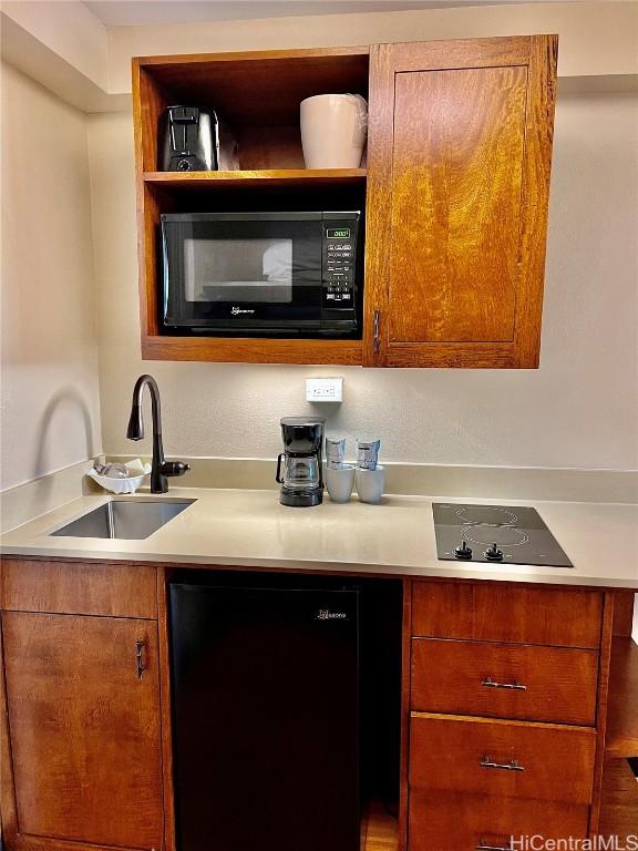 kitchen featuring brown cabinetry, light countertops, a sink, and black appliances