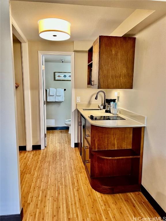 kitchen with a sink, baseboards, light countertops, light wood-type flooring, and open shelves