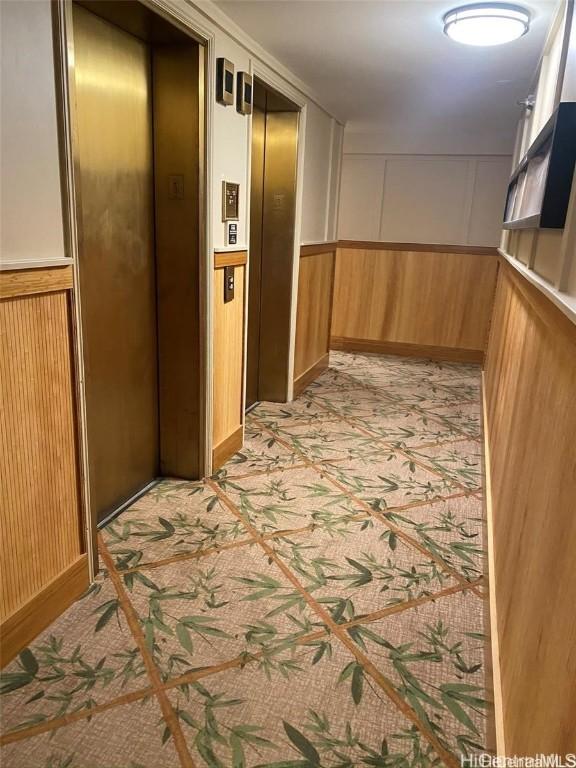 hall featuring a wainscoted wall, wood walls, light colored carpet, and elevator