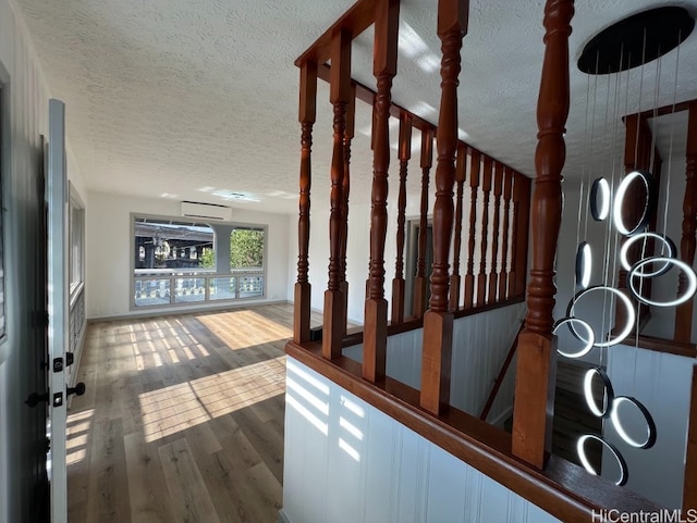 stairs with a wall unit AC, a textured ceiling, and wood finished floors