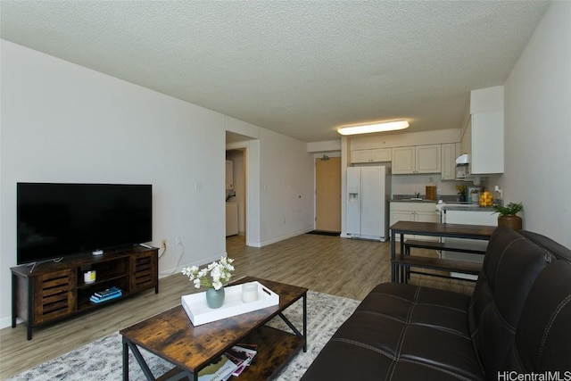 living area featuring baseboards, light wood-style flooring, and a textured ceiling