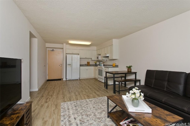 living area featuring a textured ceiling, light wood-style flooring, and baseboards