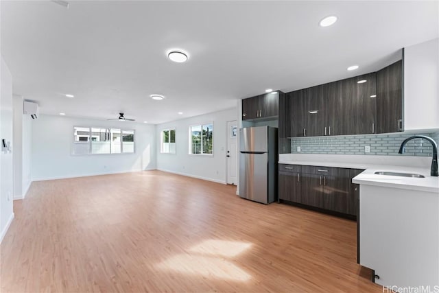 kitchen with a wall unit AC, a sink, light countertops, freestanding refrigerator, and light wood finished floors