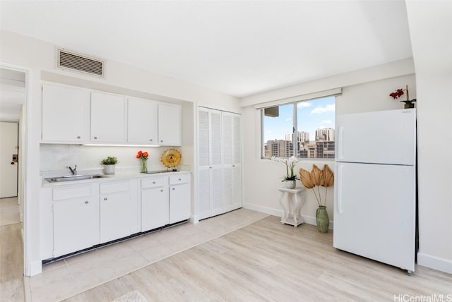 kitchen featuring a sink, visible vents, white cabinets, light countertops, and freestanding refrigerator