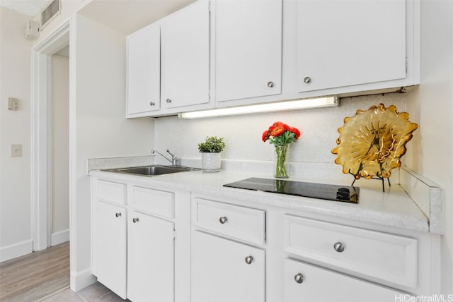 bar featuring tasteful backsplash, visible vents, a sink, baseboards, and black electric cooktop