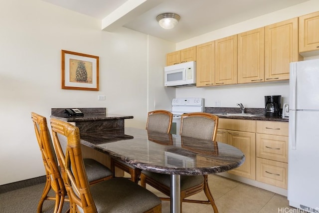 kitchen featuring dark countertops, light brown cabinets, light tile patterned flooring, white appliances, and a sink