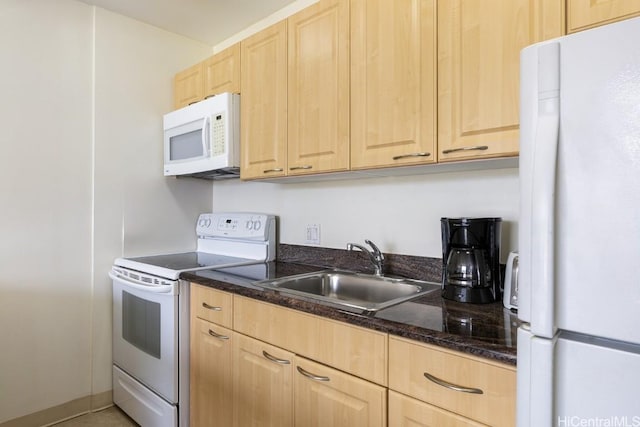 kitchen with white appliances, dark stone counters, light brown cabinets, and a sink