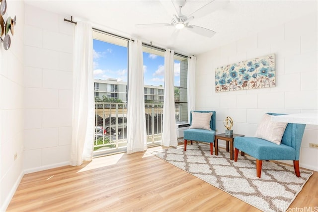 living area featuring a wall of windows, ceiling fan, and wood finished floors