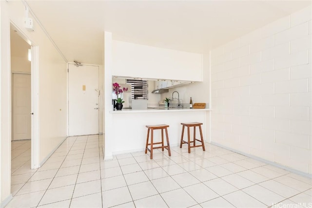 kitchen featuring light tile patterned floors, a breakfast bar, light countertops, and a sink