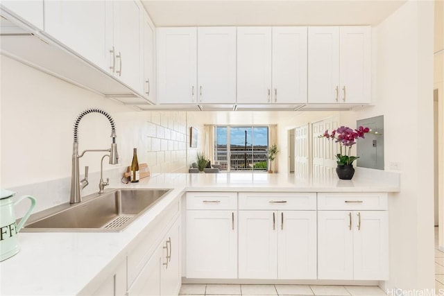 kitchen featuring a peninsula, a sink, light countertops, white cabinetry, and tasteful backsplash