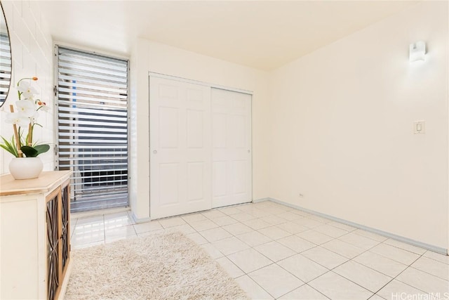 unfurnished bedroom featuring light tile patterned flooring, baseboards, and a closet