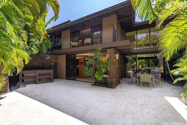 rear view of property featuring a patio, outdoor dining area, and a balcony