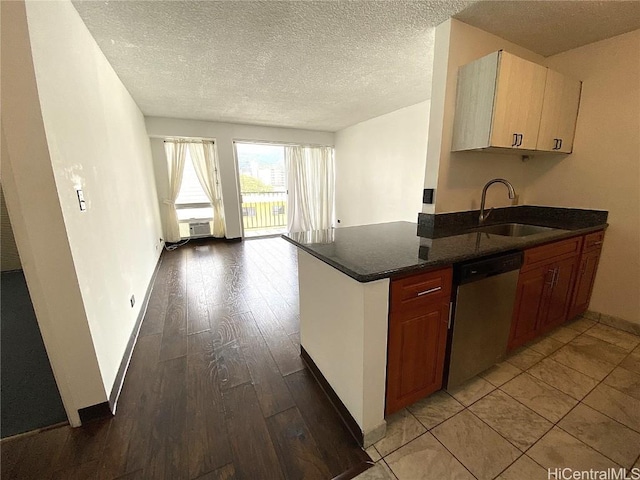 kitchen featuring dark stone countertops, stainless steel dishwasher, a textured ceiling, light wood-style floors, and a sink