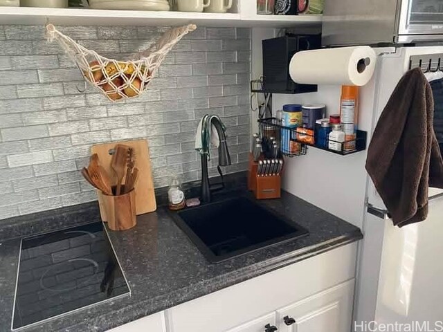 kitchen featuring tasteful backsplash, dark stone countertops, black electric stovetop, white cabinetry, and a sink