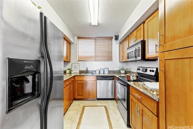 kitchen featuring light tile patterned floors, light stone countertops, stainless steel appliances, a textured ceiling, and brown cabinets