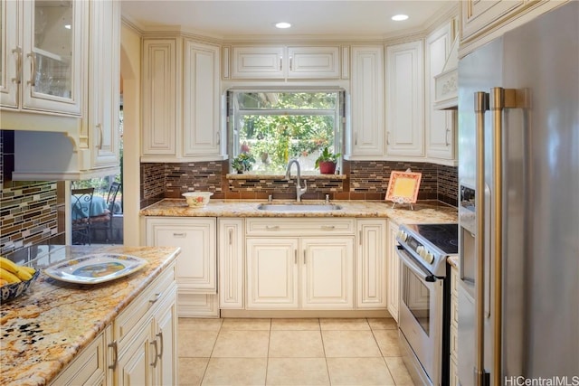 kitchen featuring light tile patterned floors, stainless steel appliances, cream cabinets, a sink, and light stone countertops