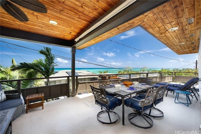 view of patio / terrace with a water view, a balcony, outdoor dining space, and a view of the beach