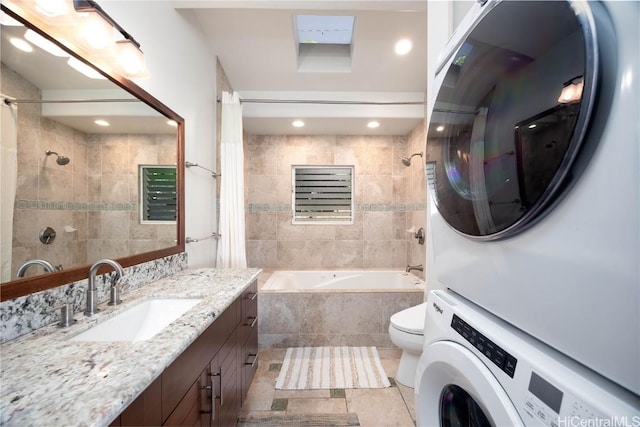 bathroom with tile patterned floors, tiled shower / bath, toilet, stacked washer and clothes dryer, and vanity