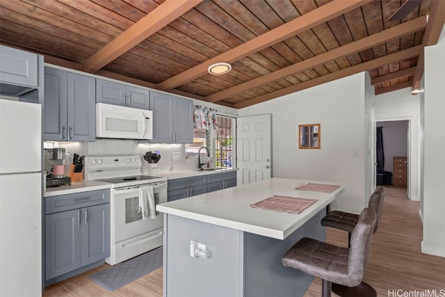 kitchen with white appliances, a breakfast bar, light countertops, gray cabinetry, and a sink