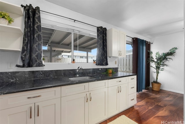 kitchen with dark stone counters, dark wood-style flooring, a sink, and white cabinetry