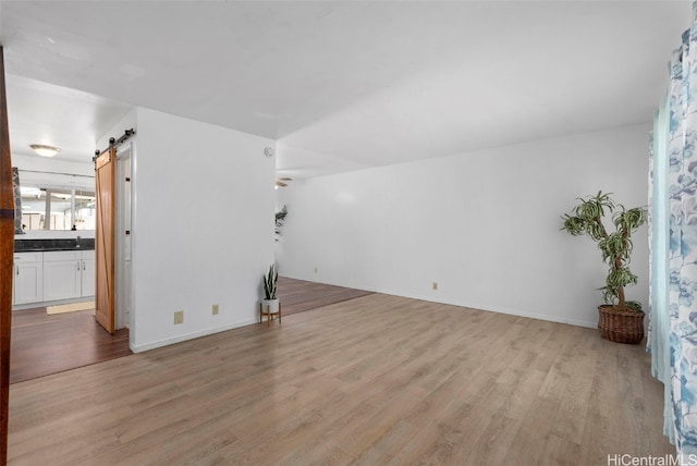 unfurnished living room featuring light wood-style flooring, baseboards, and a barn door