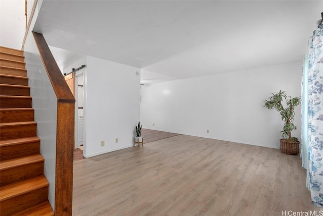 unfurnished living room featuring stairs, a barn door, light wood-style flooring, and baseboards