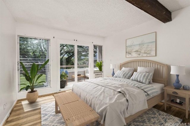 bedroom featuring a textured ceiling, wood finished floors, baseboards, access to outside, and beam ceiling