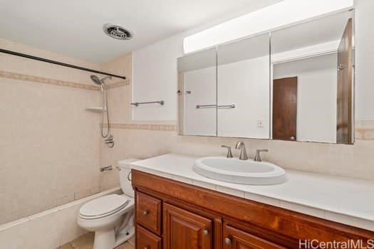 full bath with visible vents, toilet, vanity, shower / bathtub combination, and tile walls