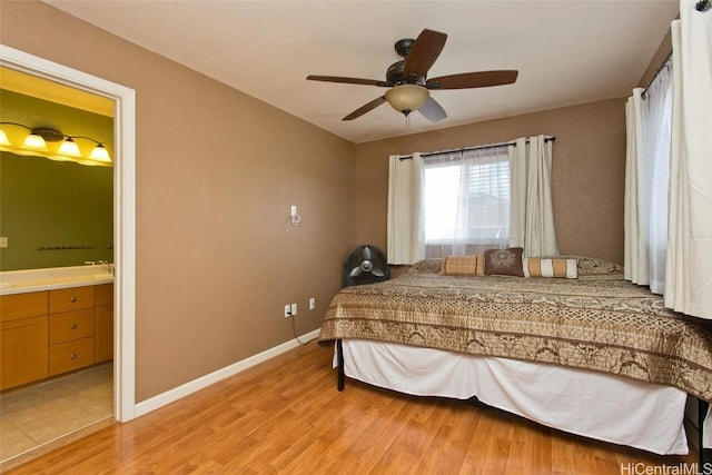 bedroom featuring baseboards, ensuite bath, a ceiling fan, and light wood-style floors