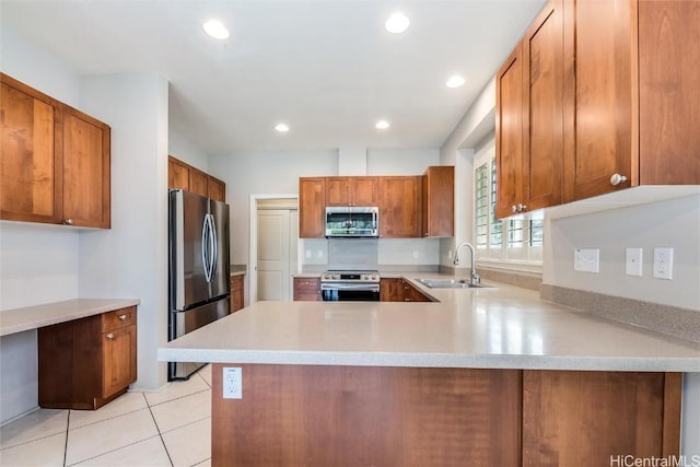 kitchen featuring stainless steel appliances, a peninsula, a sink, light countertops, and brown cabinetry