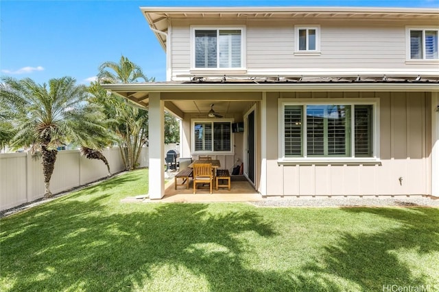 rear view of house with a ceiling fan, a fenced backyard, a yard, a patio area, and board and batten siding