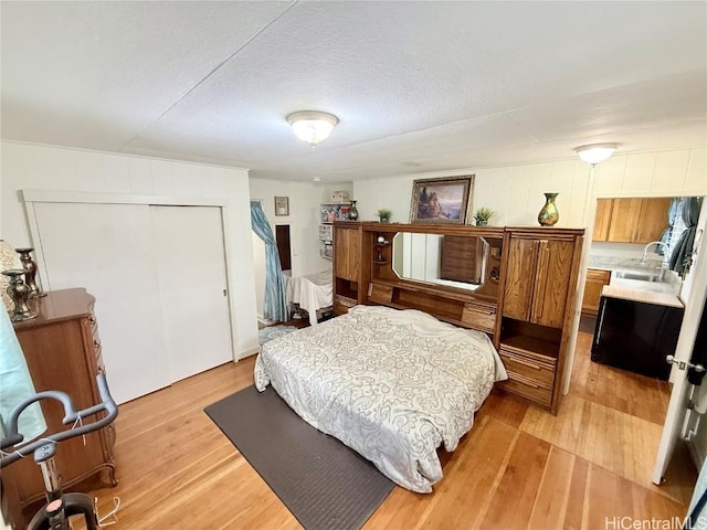 bedroom with a textured ceiling, a closet, light wood-type flooring, and a sink