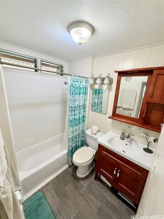 bathroom featuring a textured ceiling, toilet, wood finished floors, vanity, and shower / bath combo