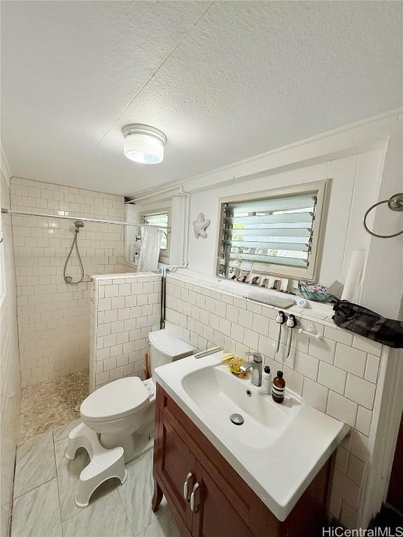 bathroom featuring tiled shower, toilet, a textured ceiling, vanity, and tile walls