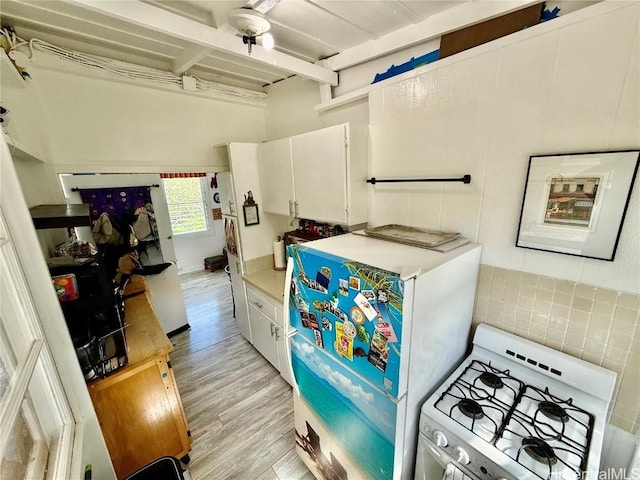 kitchen with light wood-style flooring, light countertops, fridge, white cabinetry, and gas range gas stove