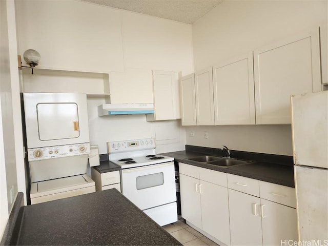 kitchen with under cabinet range hood, a sink, dark countertops, stacked washing maching and dryer, and white appliances