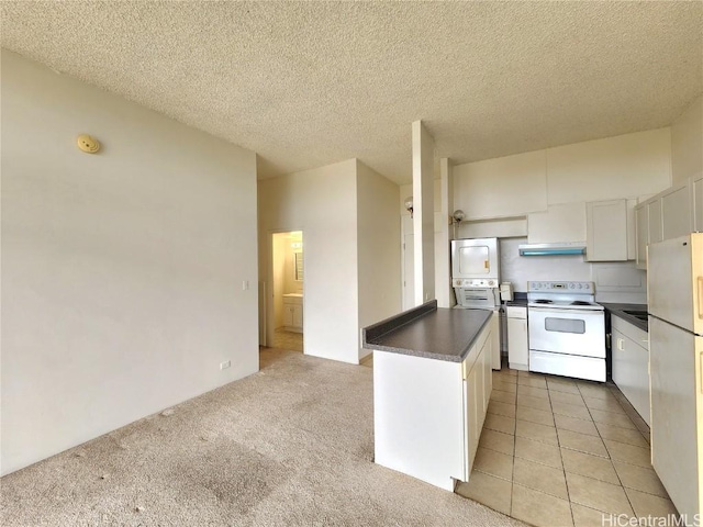 kitchen featuring dark countertops, a textured ceiling, white appliances, white cabinets, and light colored carpet