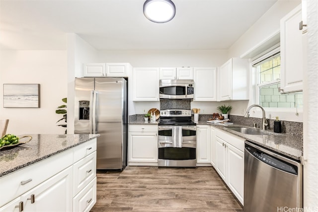 kitchen with wood finished floors, dark stone counters, a sink, white cabinets, and appliances with stainless steel finishes