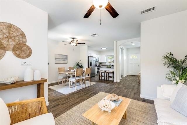 living area featuring arched walkways, visible vents, and dark wood-type flooring