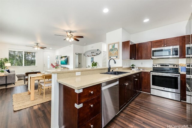 kitchen featuring dark wood-type flooring, a sink, open floor plan, stainless steel appliances, and a peninsula