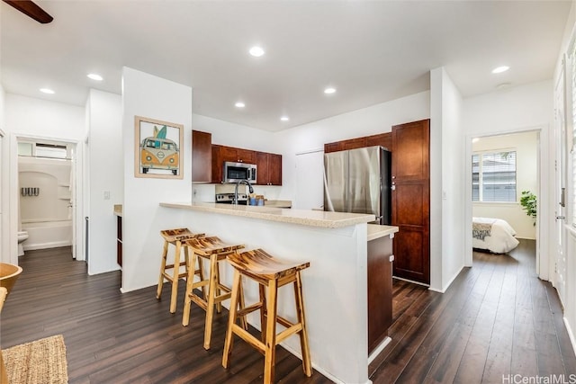 kitchen featuring stainless steel appliances, a kitchen bar, dark wood-style floors, and light countertops