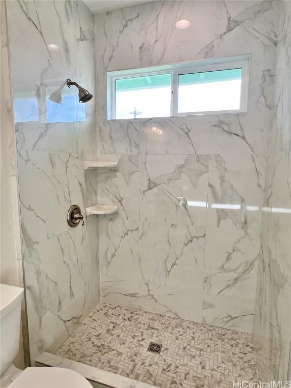 full bath with a marble finish shower and toilet